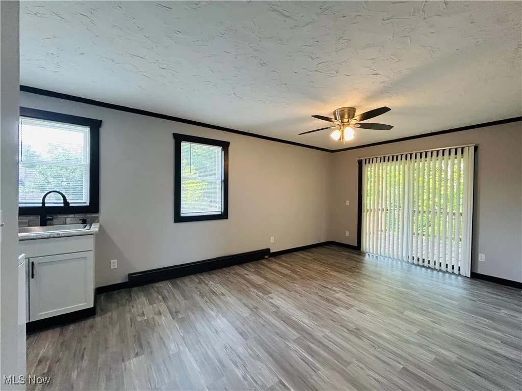 Unfurnished living room with crown molding, light wood-style flooring, healthy amount of natural light, a textured ceiling, and ceiling fan, Additional living suite.