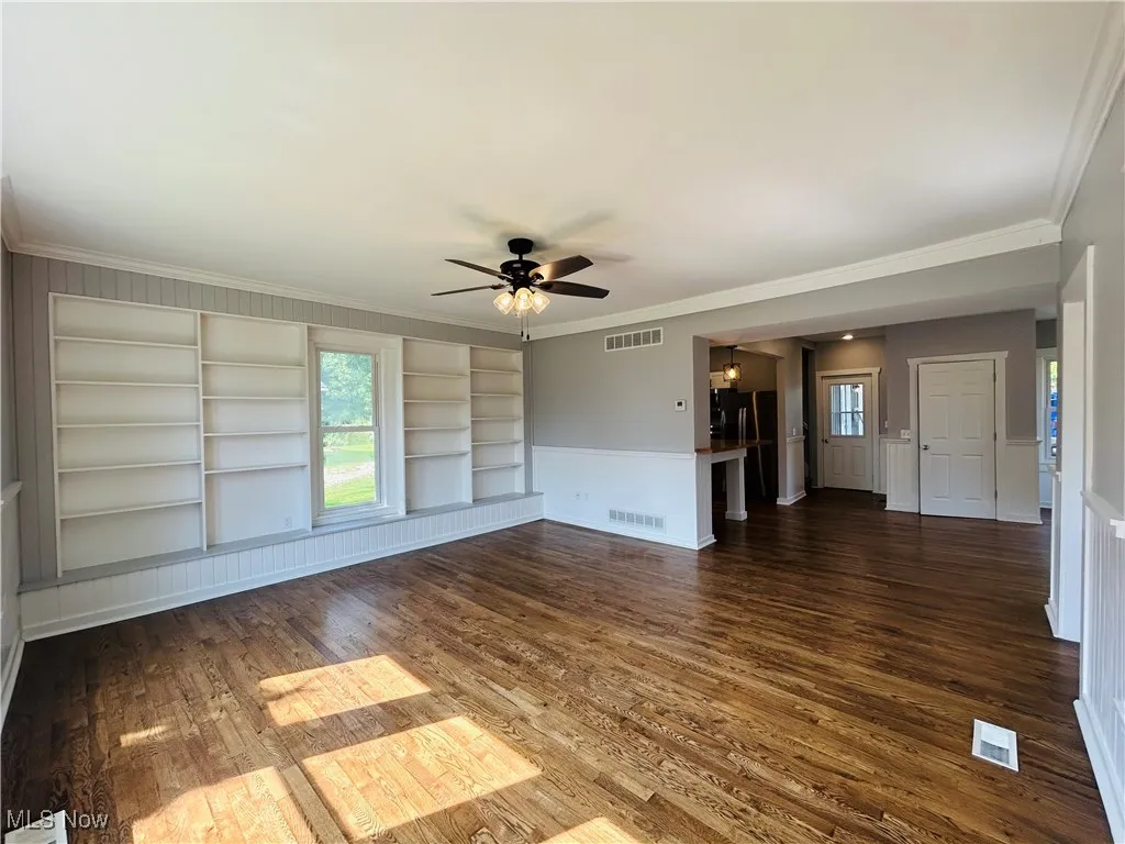 Spare room featuring built in features, ornamental molding, dark wood finished floors, and a ceiling fan