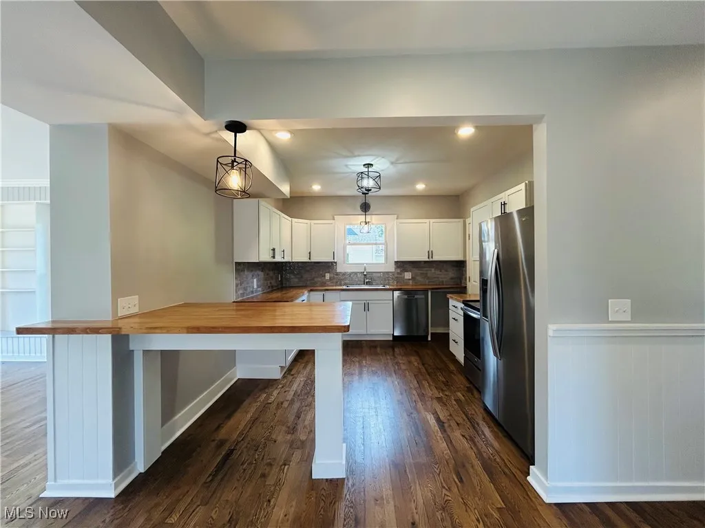 Kitchen with a peninsula, wooden counters, appliances with stainless steel finishes, dark wood-style floors, and white cabinets