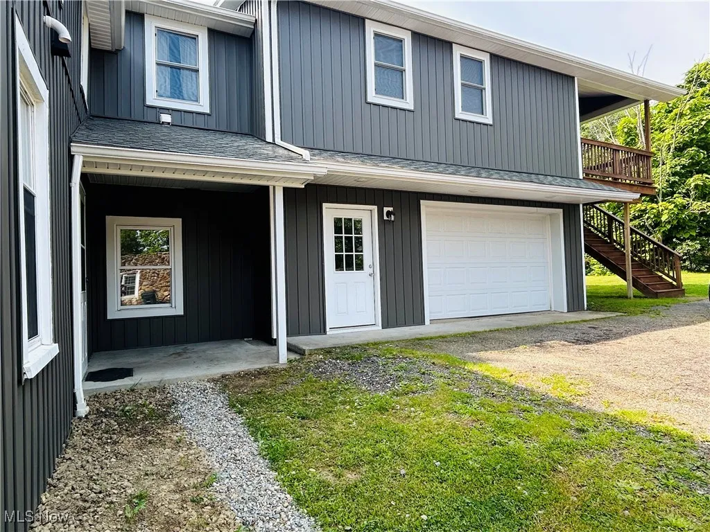 View of front of house featuring stairway, dirt driveway, a garage, a shingled roof, and board and batten siding