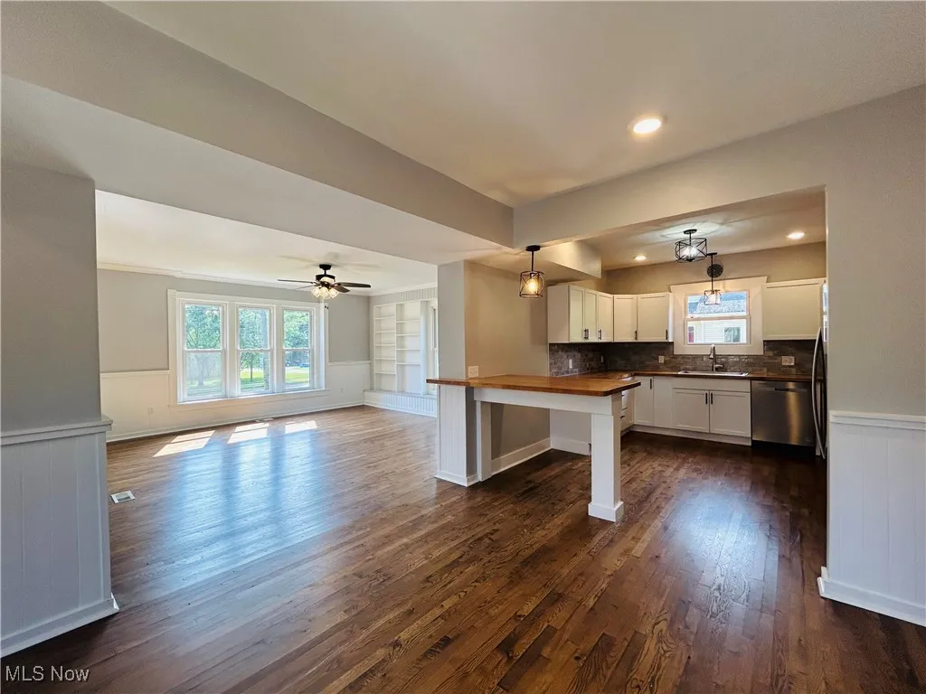 Kitchen featuring wainscoting, open floor plan, dark wood finished floors, white cabinetry, and a peninsula