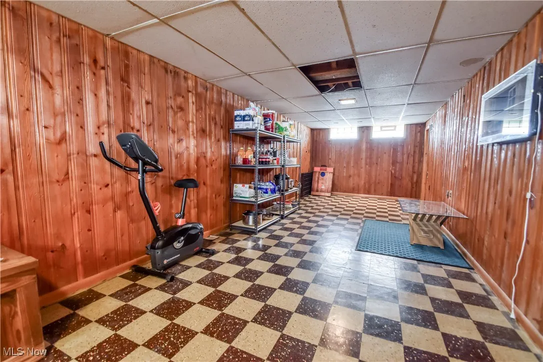 Workout area with tile patterned floors, a paneled ceiling, and wood walls