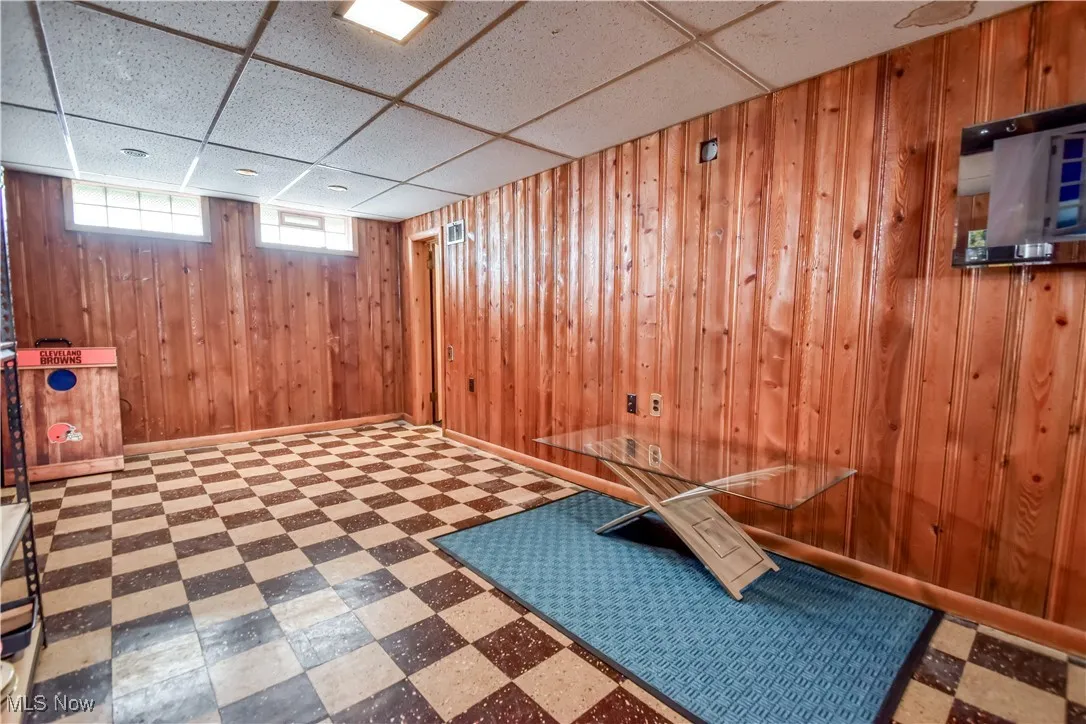 Basement with tile patterned floors, a drop ceiling, and wooden walls