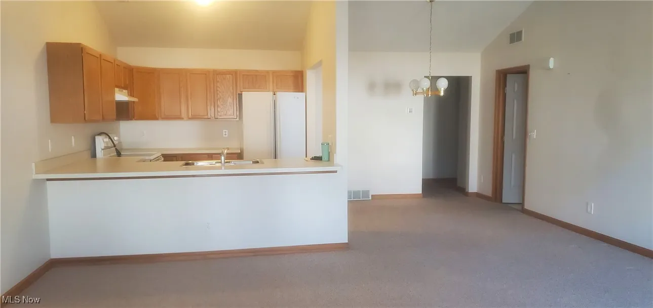 Kitchen featuring freestanding refrigerator, carpet floors, range, light countertops, and vaulted ceiling