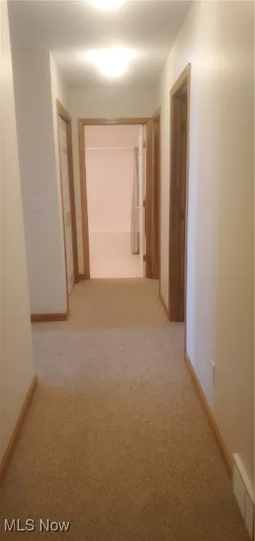 Hallway featuring light colored carpet and baseboards