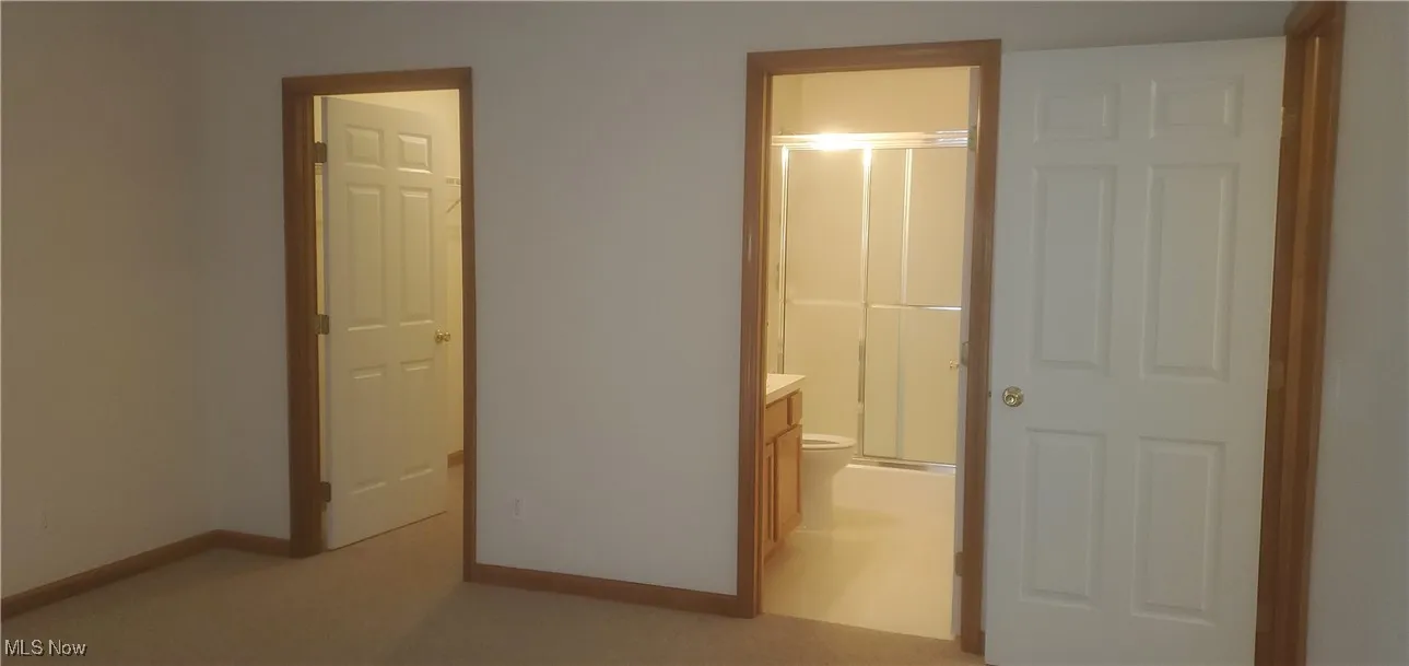 Unfurnished bedroom with ensuite bathroom and light colored carpet