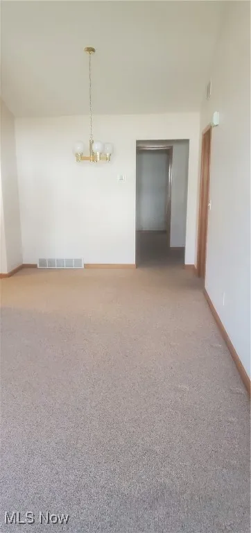 Carpeted spare room with baseboards and a chandelier