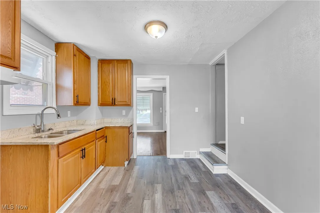 Kitchen with light wood-type flooring, a textured ceiling, light stone counters, and brown cabinets