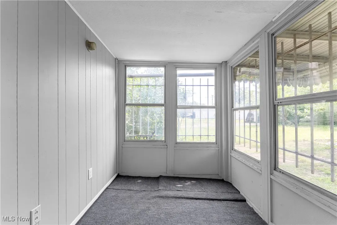 Unfurnished sunroom featuring wooden walls, a textured ceiling, and carpet