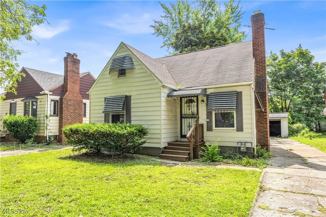 Bungalow-style home with a shingled roof, a front yard, and an outbuilding
