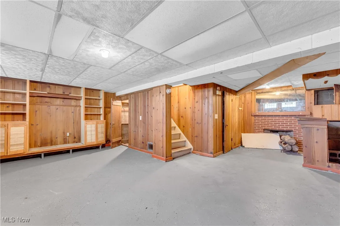 Finished basement with a paneled ceiling, stairway, and wooden walls