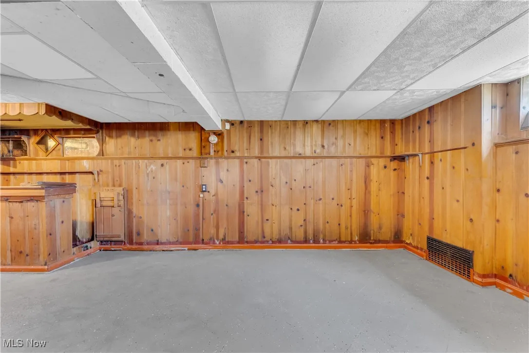 Finished basement with wood walls, a paneled ceiling, and a bar