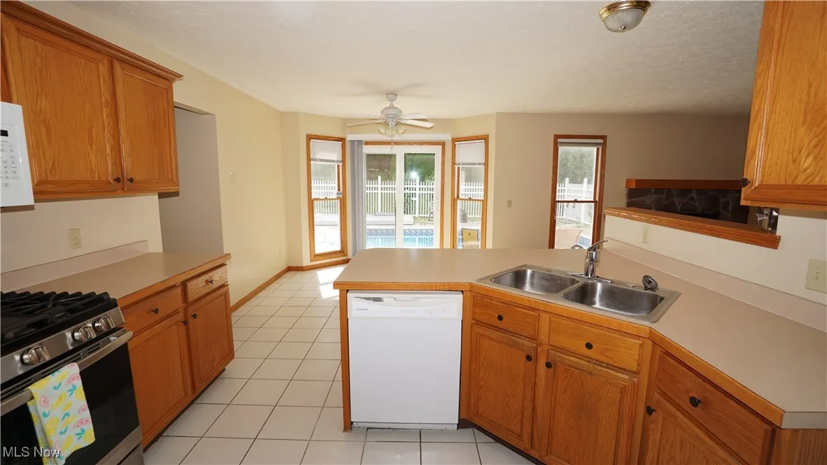 Kitchen with a peninsula, white appliances, light countertops, ceiling fan, and light tile patterned floors