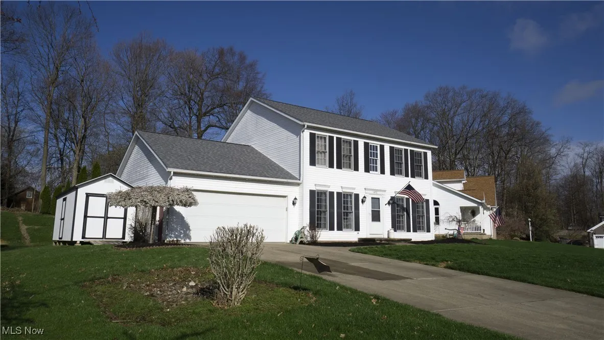 View of side of property with roof with shingles, a lawn, driveway, a garage, and a storage unit