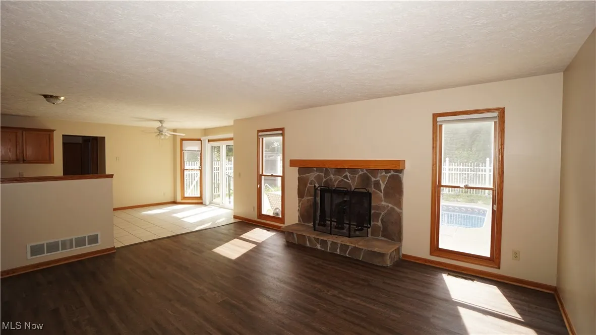 Unfurnished family room with a textured ceiling, a stone fireplace, wood finished floors, and ceiling fan