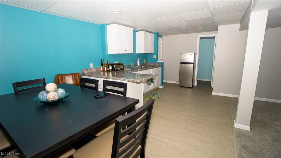 Kitchen in basement featuring freestanding refrigerator, light wood-style floors, white cabinets, a paneled ceiling, and dark countertops