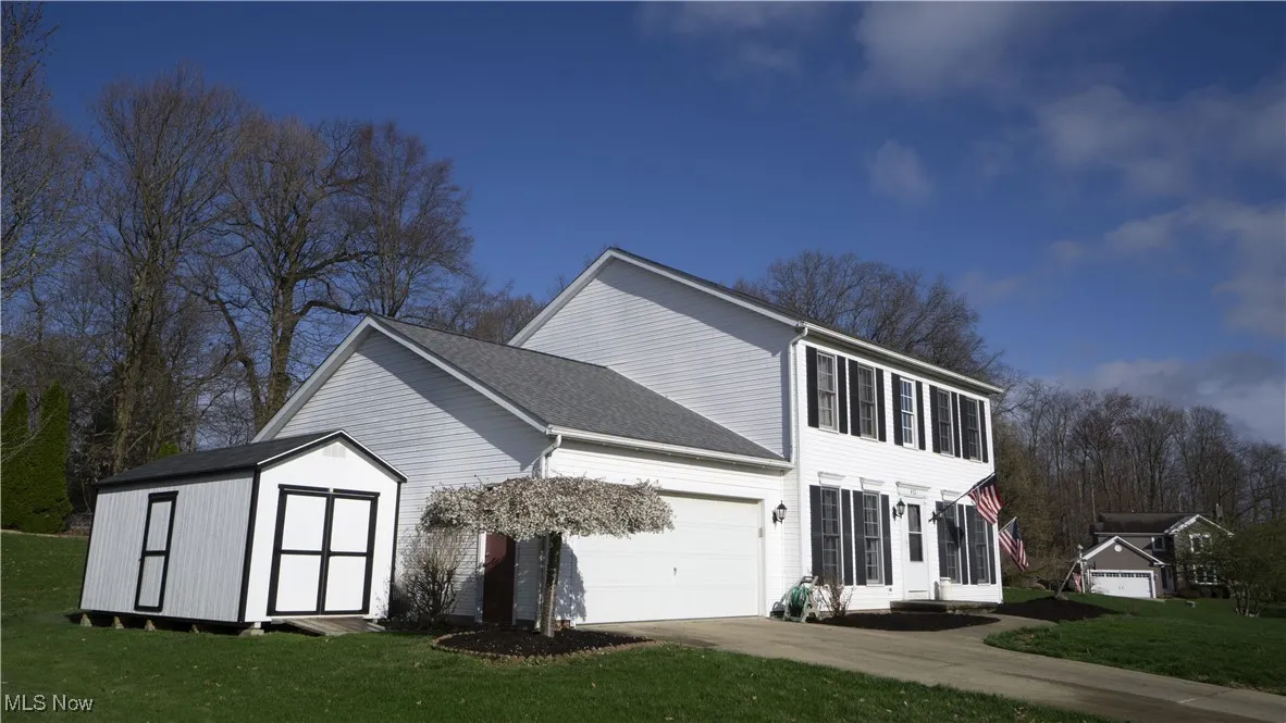 View of home's exterior with a lawn, an attached garage, driveway, a shed, and roof with shingles