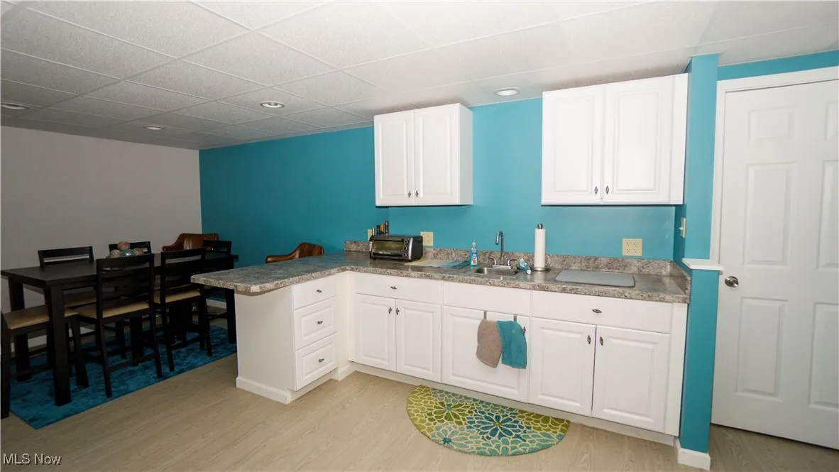 Basement kitchen featuring light wood-style floors, white cabinetry, a peninsula, and a paneled ceiling