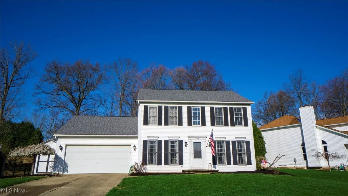 Colonial-style house with a front lawn, concrete driveway, an attached garage, and a shingled roof