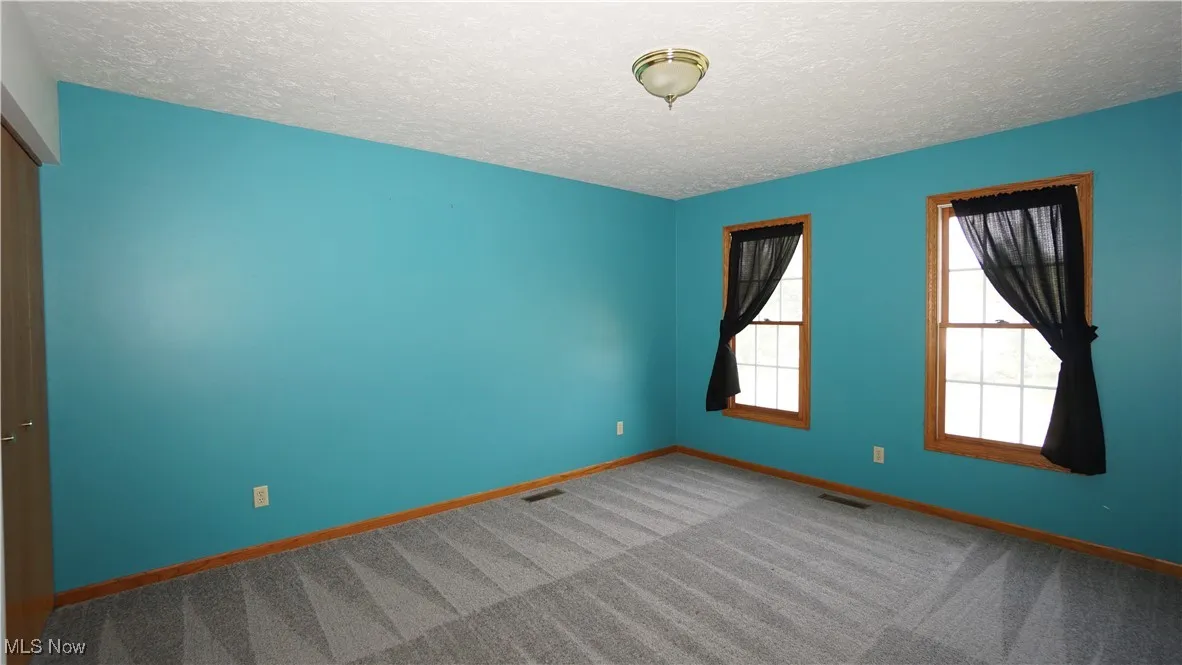 Carpeted spare room with a textured ceiling and baseboards