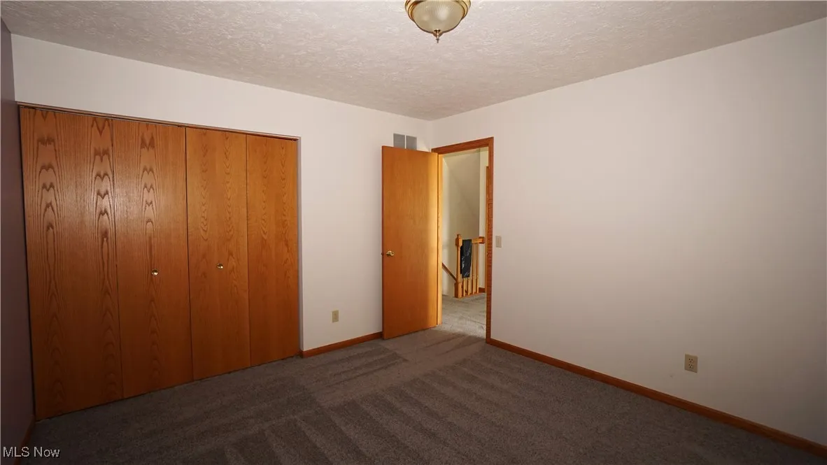 Unfurnished bedroom with dark carpet, a textured ceiling, and a closet