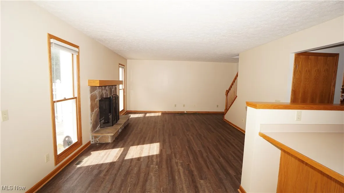 Unfurnished family room with dark wood-type flooring, a textured ceiling, a fireplace, and stairs