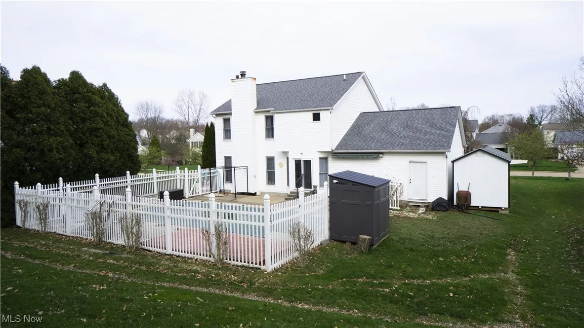 Rear view of house with a shed, roof with shingles, a fenced backyard, and a chimney