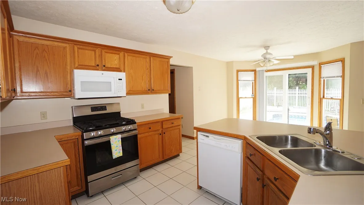 Kitchen featuring white appliances, light countertops, brown cabinets, a ceiling fan, and a textured ceiling