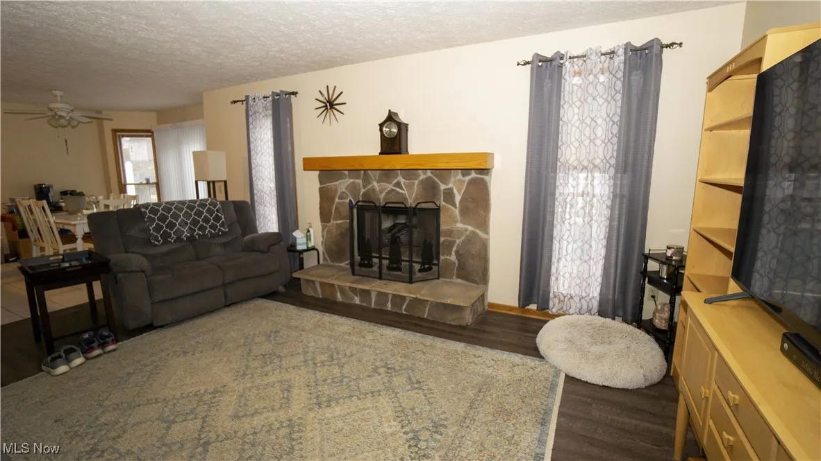 Family room featuring a textured ceiling, a stone fireplace, wood finished floors, and ceiling fan