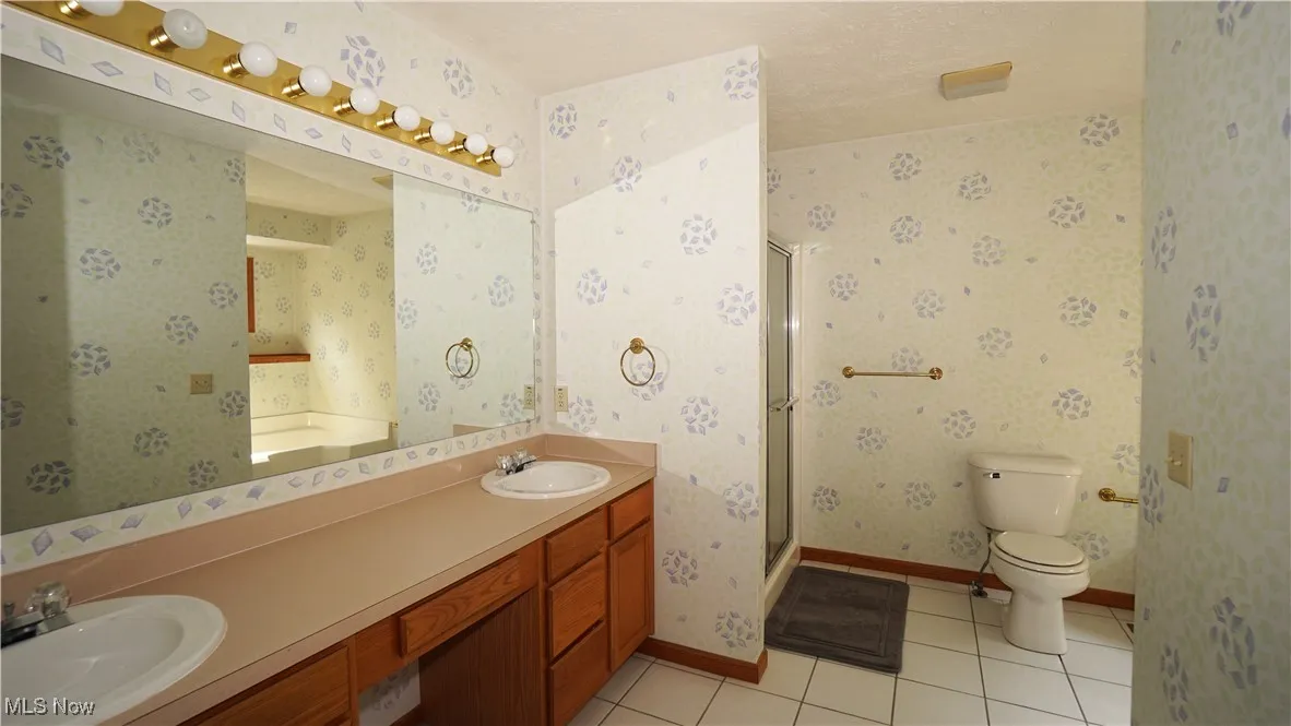 Primary bathroom with tile patterned floors, a shower stall, double vanity, wallpapered walls, and a bathtub