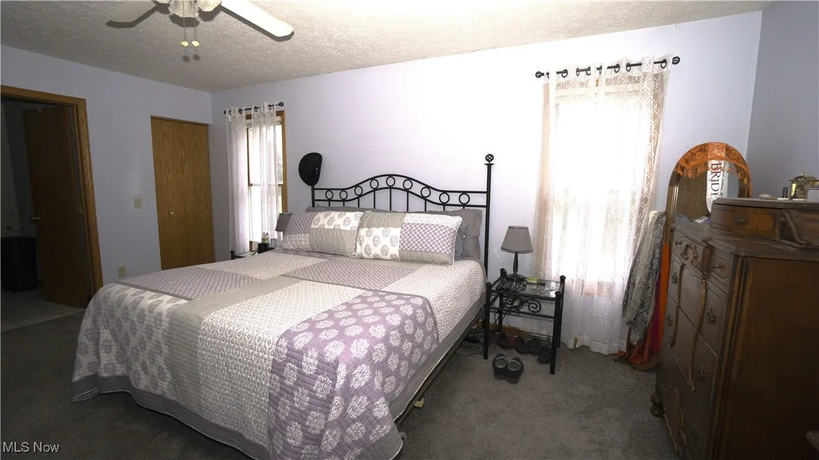 Carpeted Primary bedroom featuring a textured ceiling, two closets, and a ceiling fan