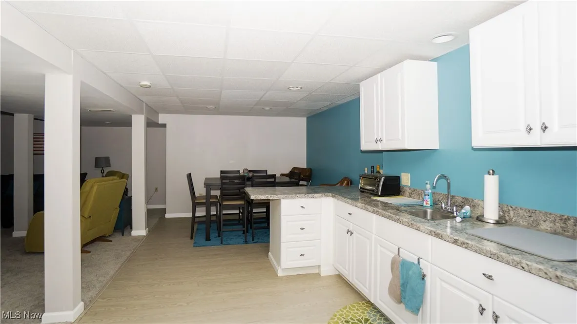 Kitchen in basement featuring light wood-type flooring, white cabinetry, a peninsula, and a paneled ceiling