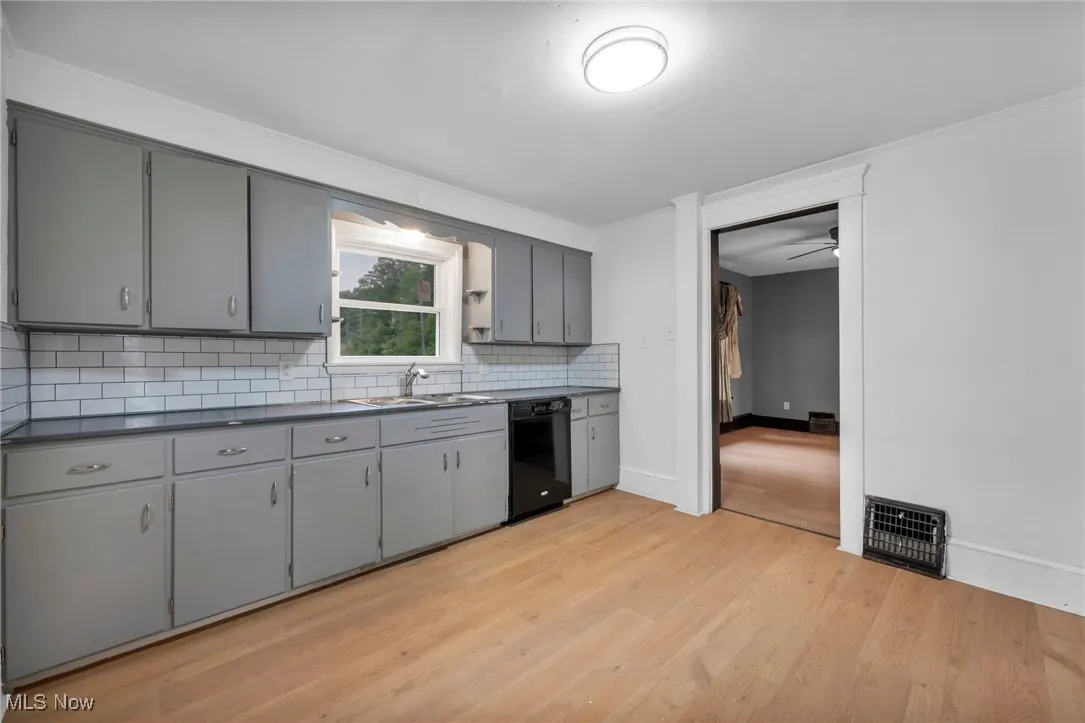 Kitchen featuring gray cabinets, dark countertops, light wood finished floors, tasteful backsplash, and ornamental molding