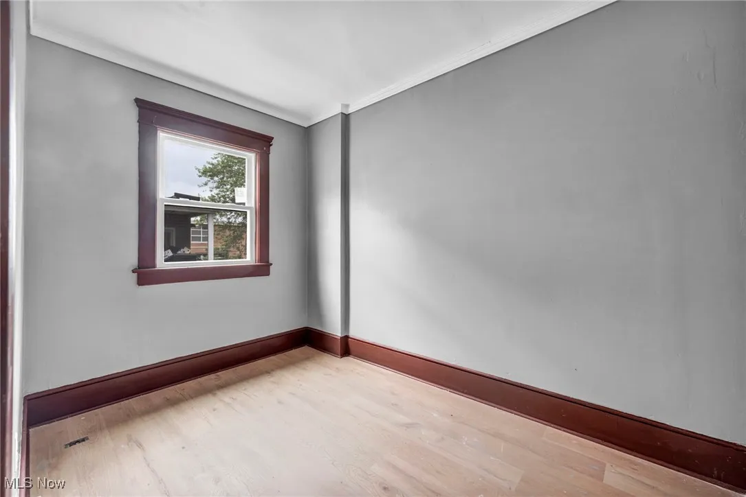 Empty room featuring wood finished floors and crown molding
