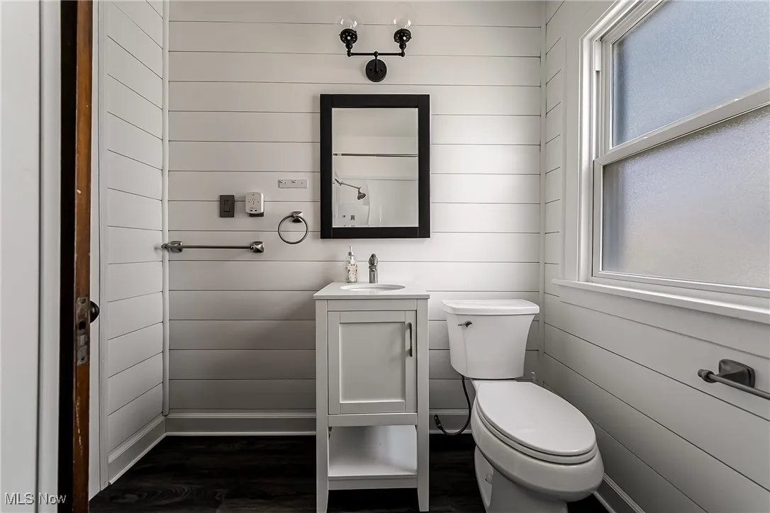 Half bath featuring wooden walls, vanity, and wood finished floors