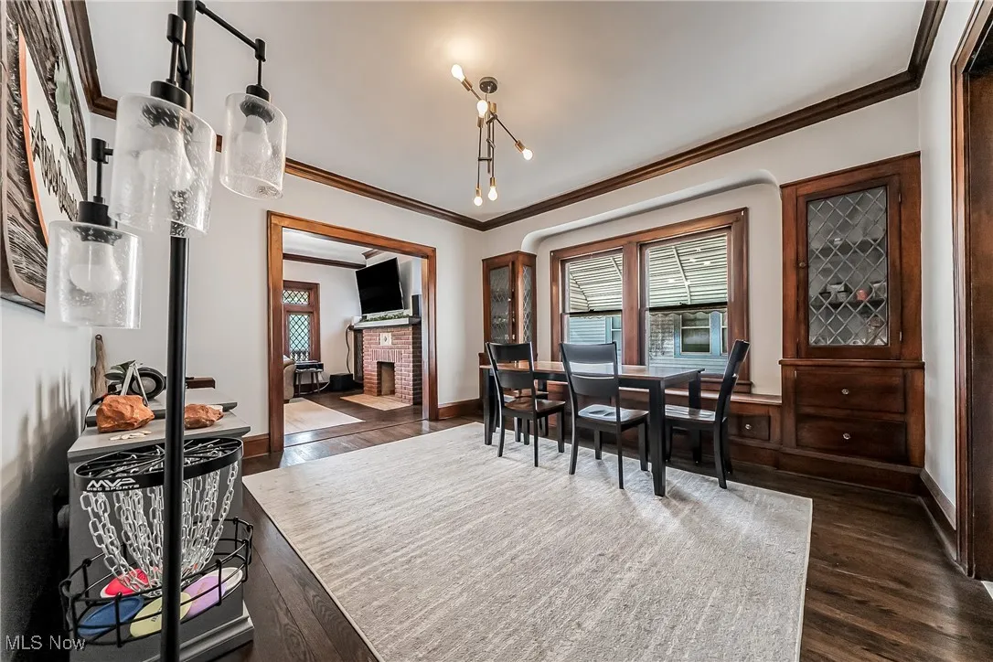 Dining area with ornamental molding, dark wood-style flooring, and a brick fireplace