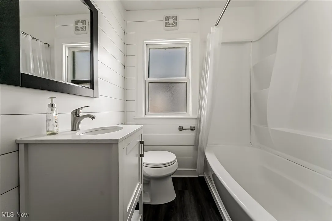 Bathroom with vanity, wood finished floors, wooden walls, and shower / tub combo
