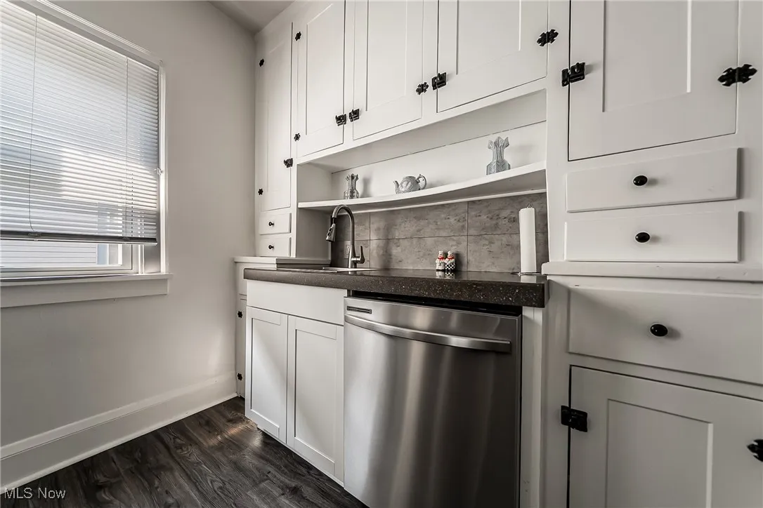 Kitchen with open shelves, stainless steel dishwasher, dark wood-style floors, white cabinetry, and backsplash