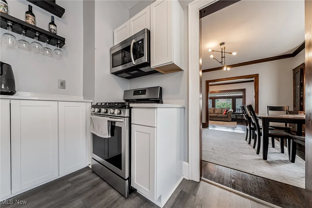 Kitchen featuring stainless steel appliances, white cabinetry, a chandelier, ornamental molding, and dark wood-style flooring