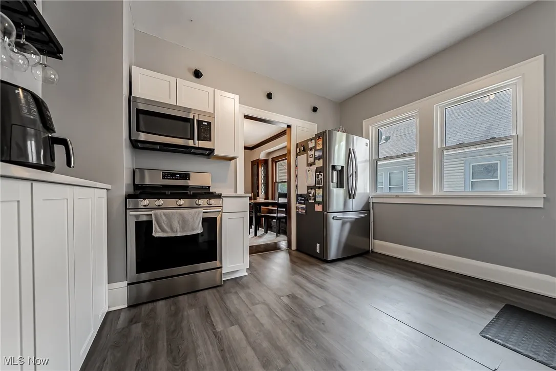 Kitchen featuring appliances with stainless steel finishes, white cabinetry, dark wood-type flooring, and light countertops