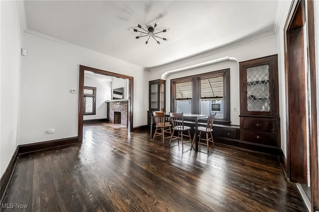 Dining room featuring crown molding, dark wood finished floors, a brick fireplace, and a chandelier