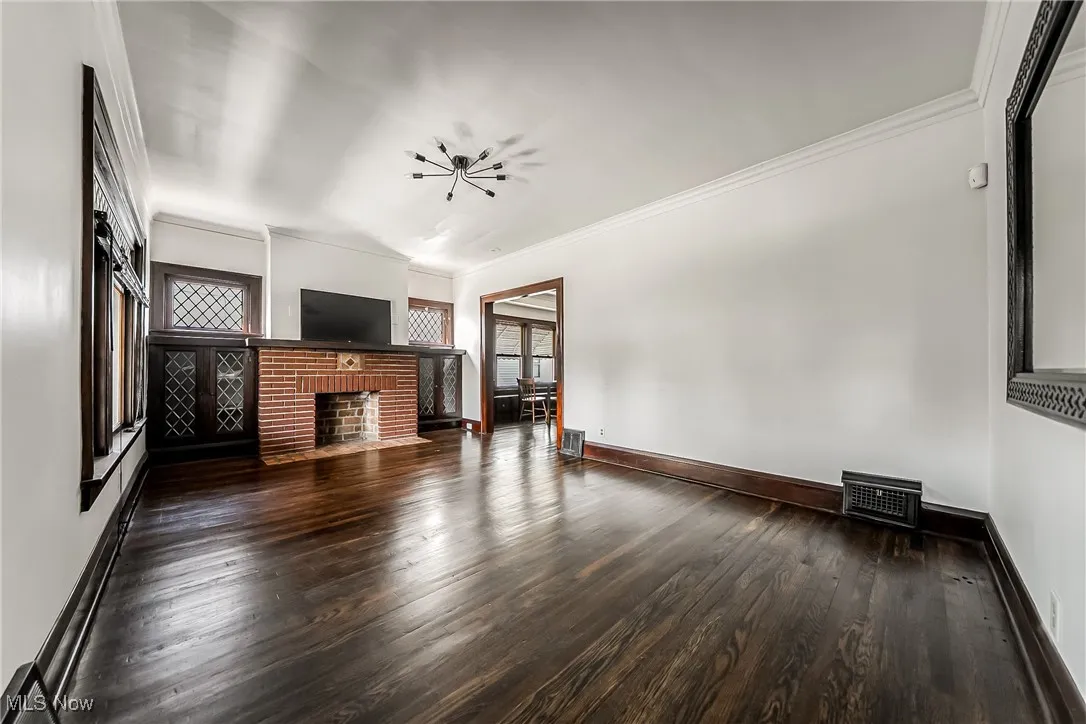 Unfurnished living room featuring wood finished floors, crown molding, healthy amount of natural light, and a fireplace