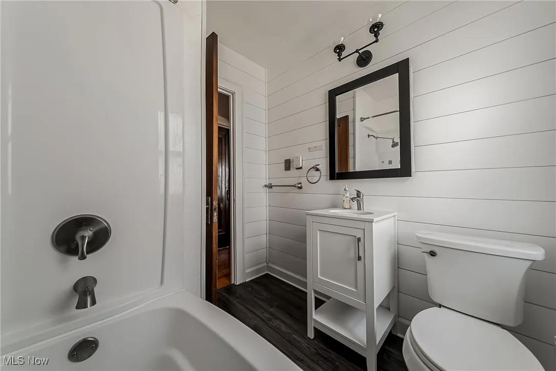 Full bathroom with wood finished floors, vanity, wooden walls, and bathtub / shower combination