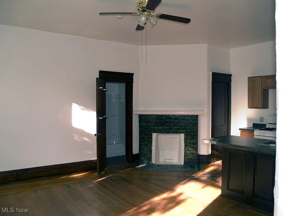 Unfurnished living room featuring wood finished floors, a fireplace with raised hearth, and a ceiling fan