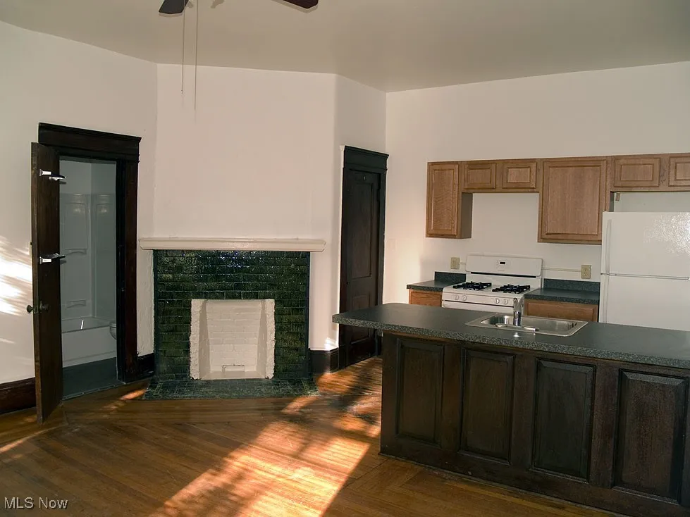 Kitchen featuring white appliances, dark countertops, dark wood-style floors, and a fireplace with flush hearth