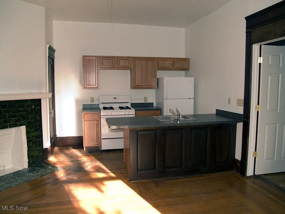 Kitchen with white appliances, a peninsula, dark countertops, a brick fireplace, and parquet floors