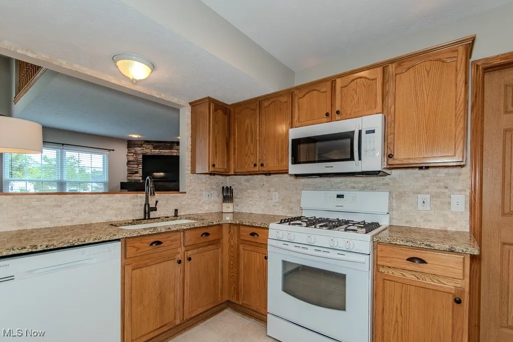 Kitchen featuring white appliances, decorative backsplash, a textured ceiling, light tile patterned floors, and light stone countertops