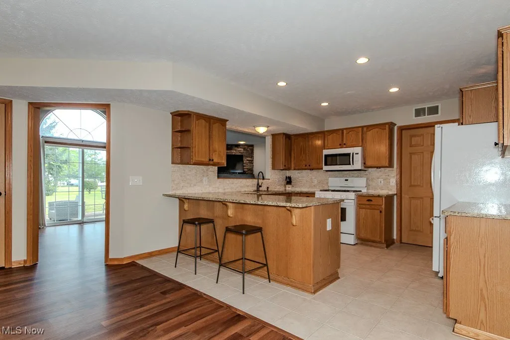 Kitchen with backsplash, white appliances, brown cabinetry, light wood finished floors, and recessed lighting