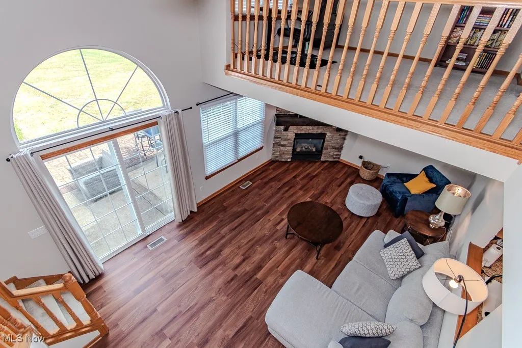 Living room with wood finished floors, a high ceiling, and a stone fireplace