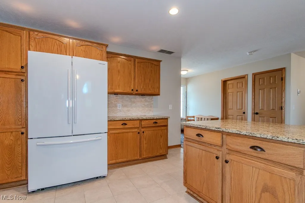 Kitchen with freestanding refrigerator, light stone counters, brown cabinetry, tasteful backsplash, and recessed lighting